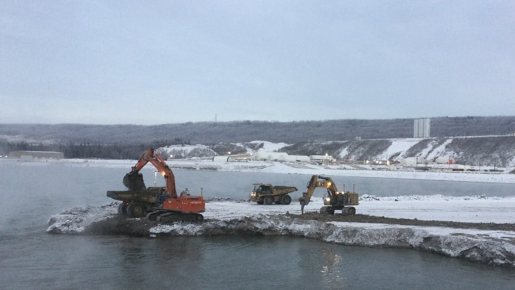 Excavators working on a snowy island in a river.