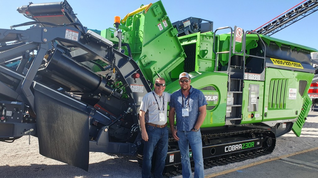 Two people stand for a photo near an impact crusher