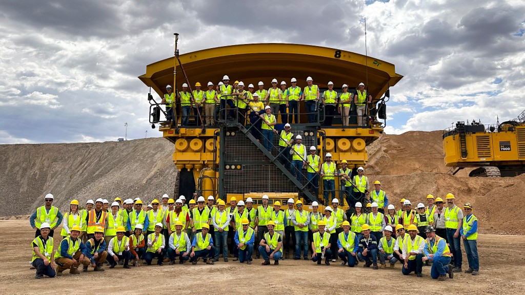 A group of people stand on and around a mining truck for a photo