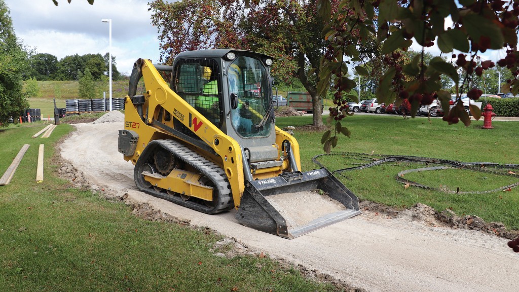 A compact track loader travels down a narrow path