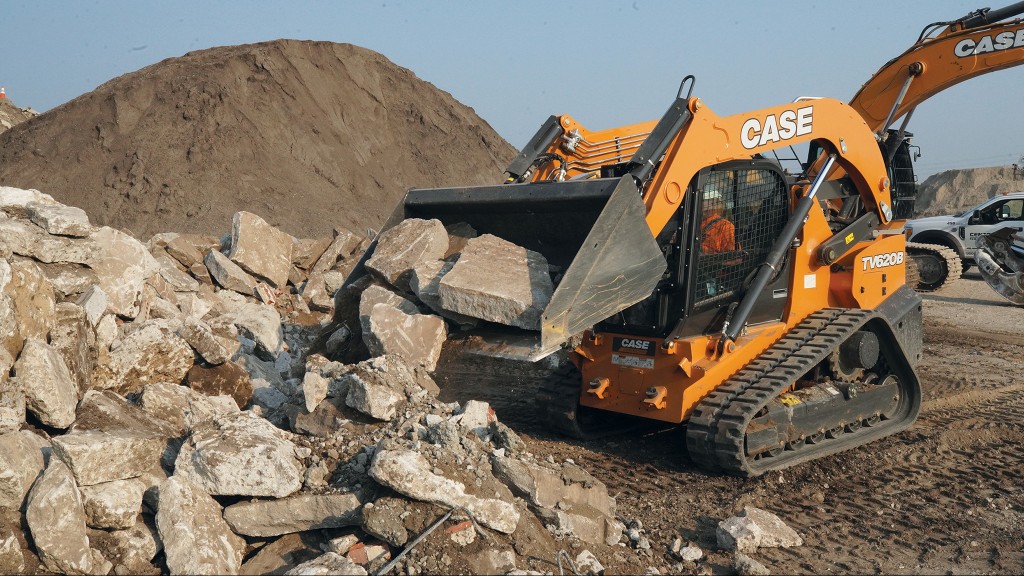 A compact track loader dumps a bucket of rocks onto a pile