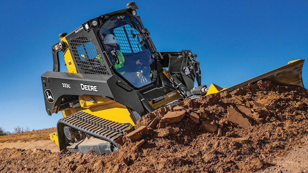 A compact track loader pushes a large pile of dirt