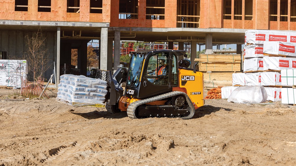 A compact track loader transports a pallet of bagged concrete