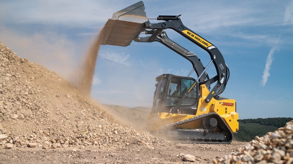 A compact track loader dumps out a bucket of gravel onto a pile