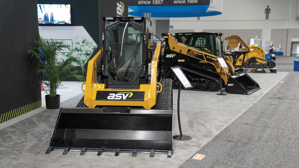 Two compact track loaders are parked on the floor of a trade show booth