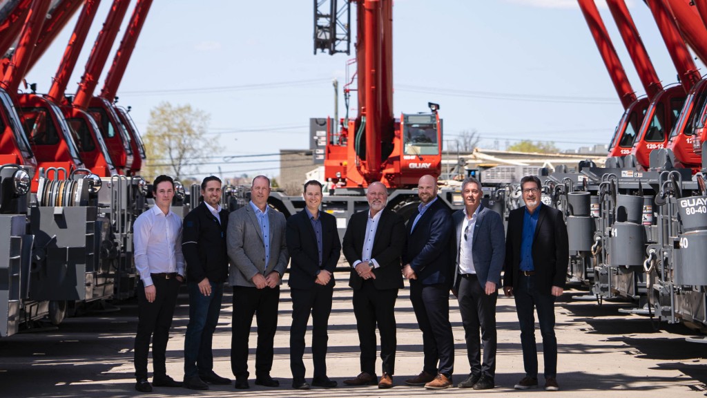 A group of people stand below the booms of multiple rough-terrain cranes