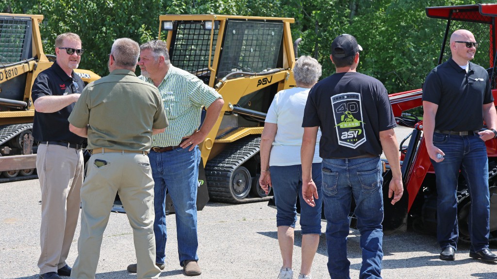 A group of people mill about near several compact track loaders
