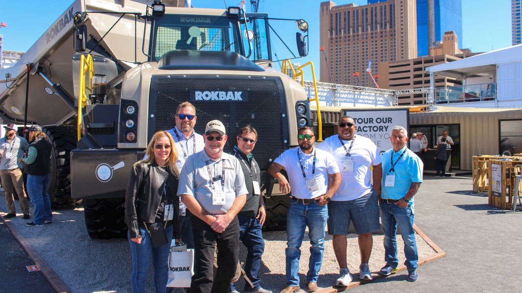 Several people pose near an articulated hauler for a photo