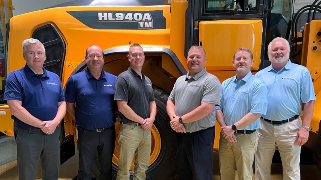 A group of people standing next to one another in front of a loader.