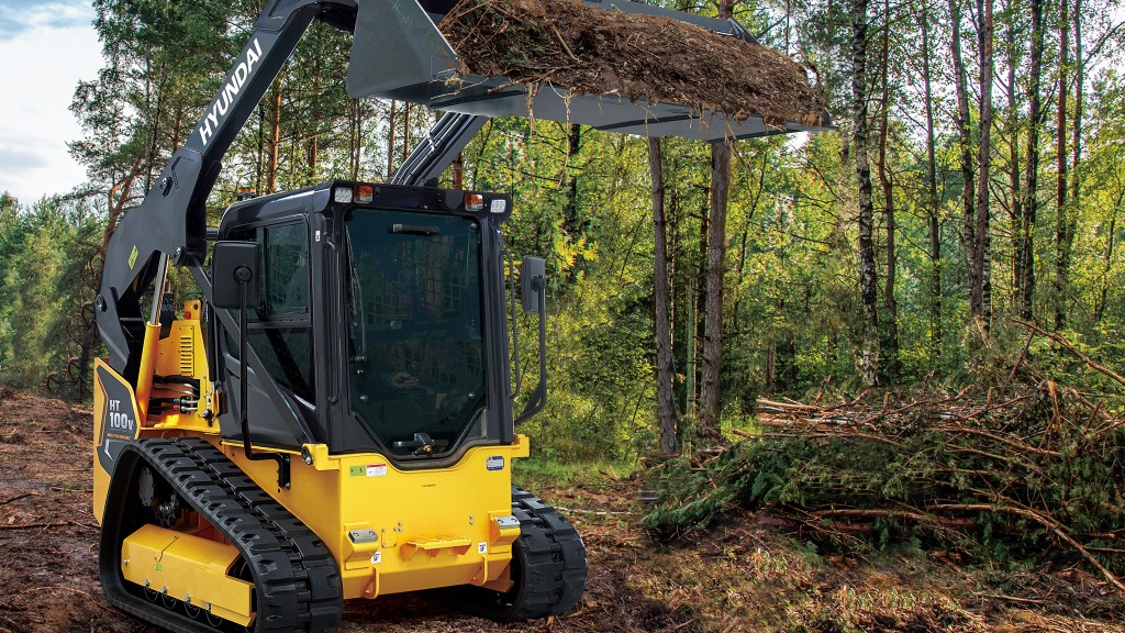 A compact track loader working in woods.