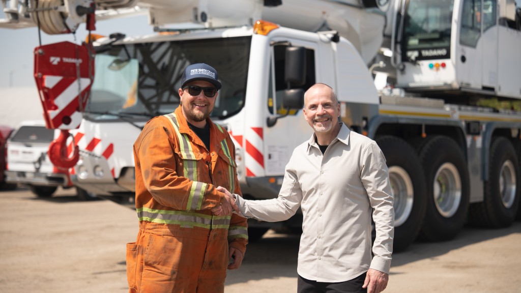 Two people shake hands near an all-terrain crane