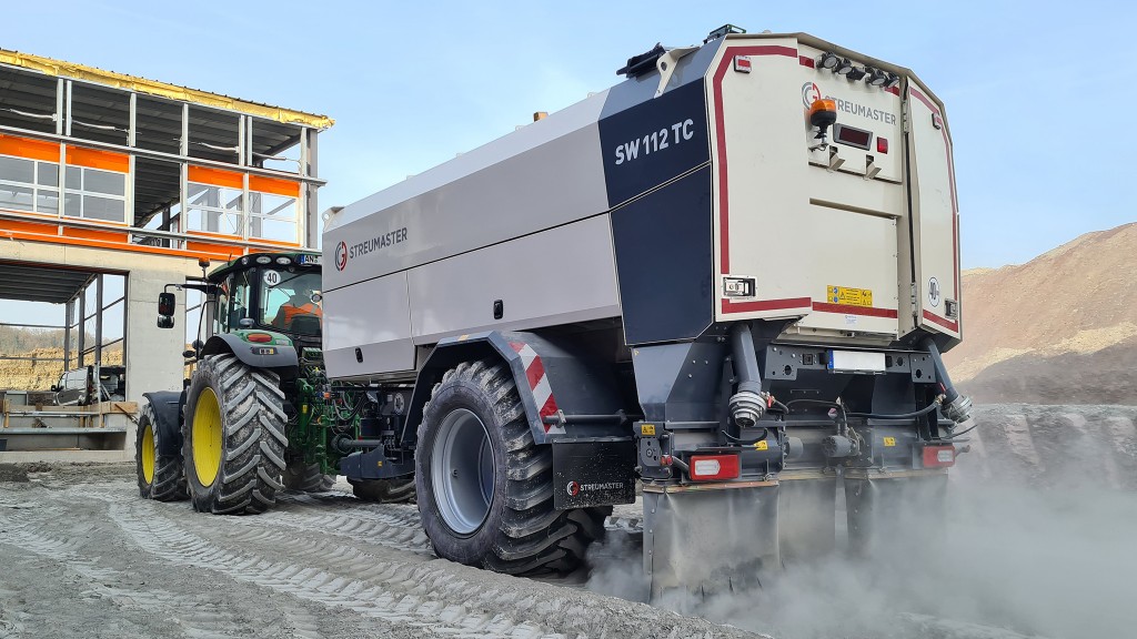 A binding agent spreader on a trailer being towed by a tractor.