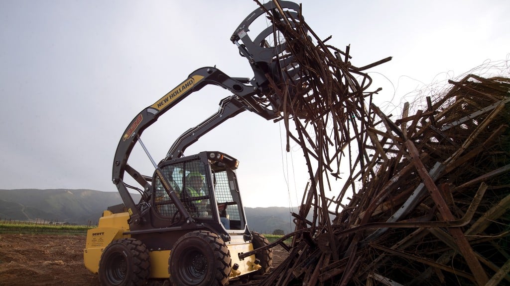 A skid-steer loader grabs pieces of metal in a grapple attachment