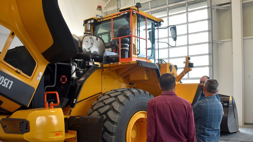 A group of people looking over a large wheel loader in a training bay
