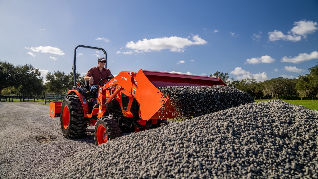 A compact tractor scooping gravel from a pile.