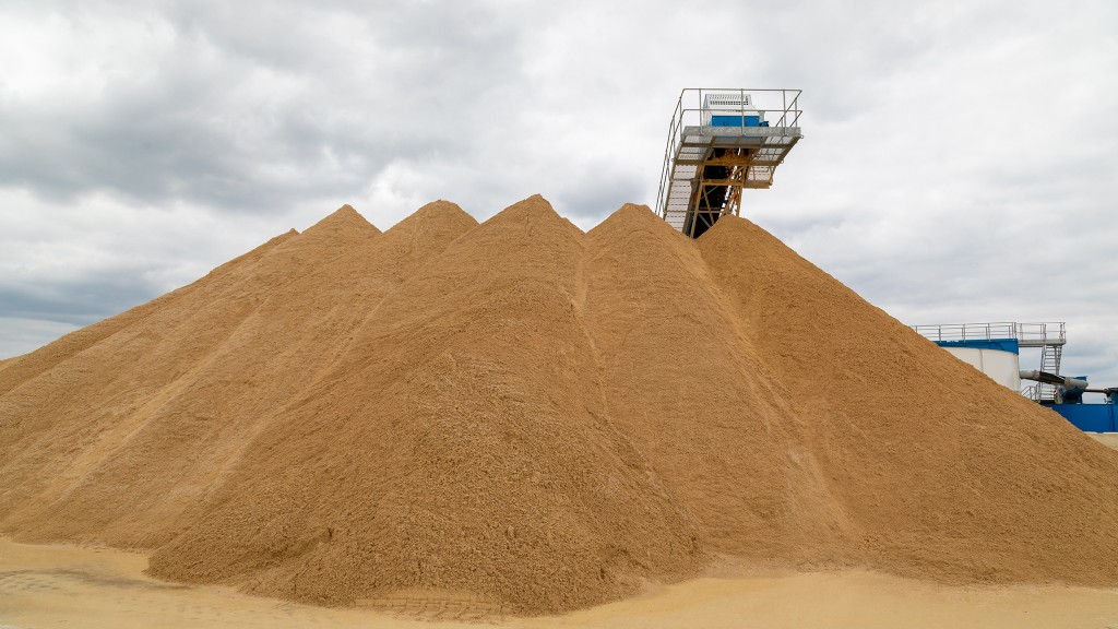 A mound of sand in a quarry with a conveyor appearing behind it.