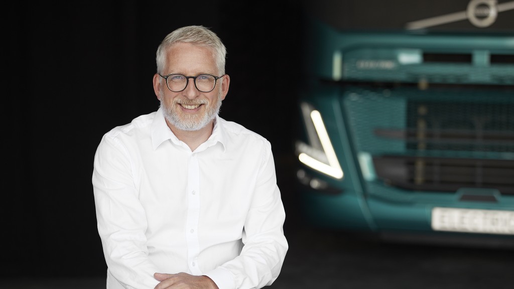 A man sitting in front of a large truck and a dark background.