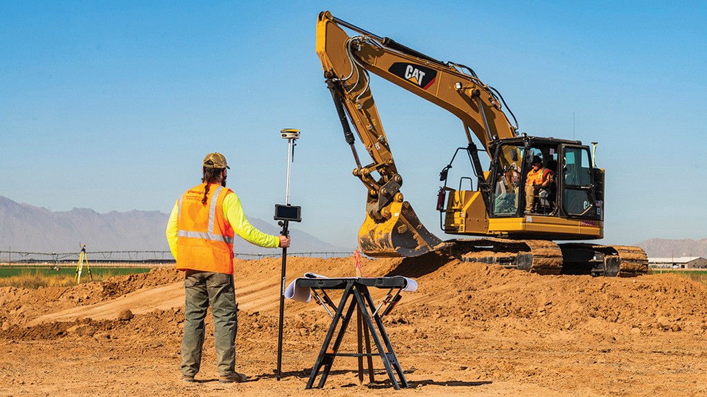 A worker using GNSS tools in front of an excavator.