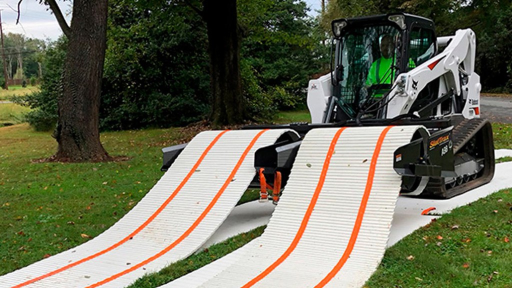 A compact track loader unrolling temporary road surface on grass.