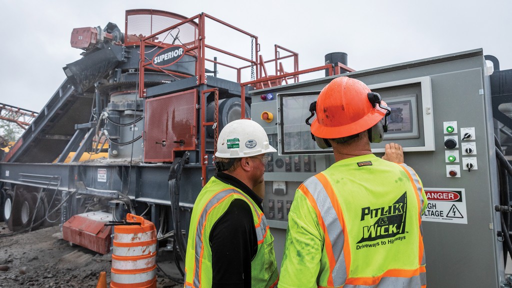 Two operators look at the controls of a cone crusher