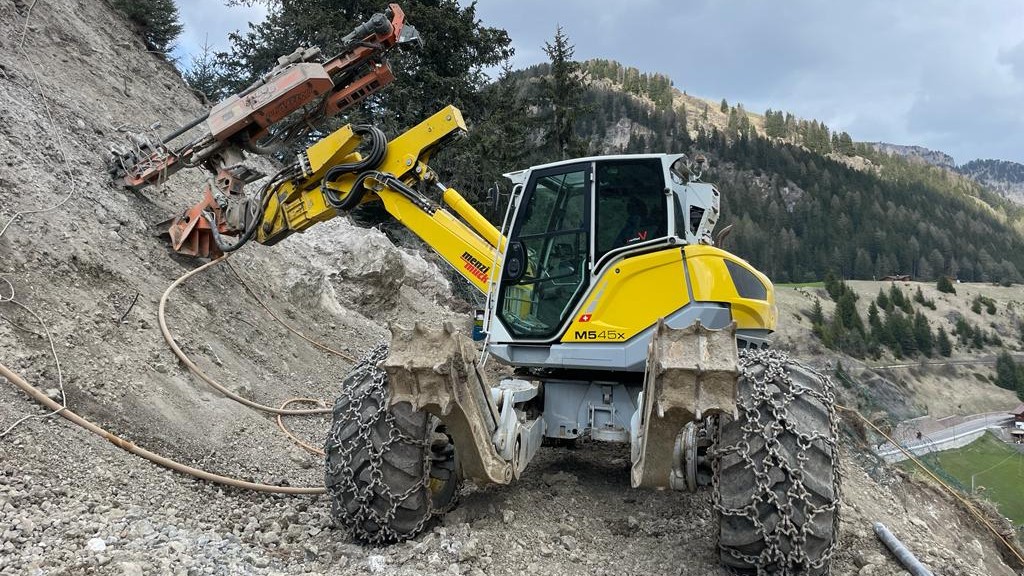 A spider excavator uses a breaker on the side of a rock face