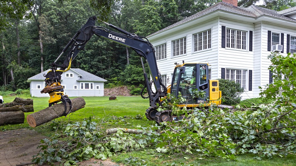 An excavator with a tiltrotator and timber grapple in front of a house.