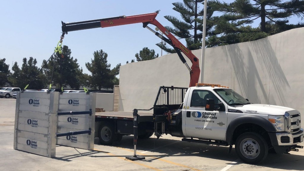 A crane mounted on a flatbed pickup unloading a trench box structure.