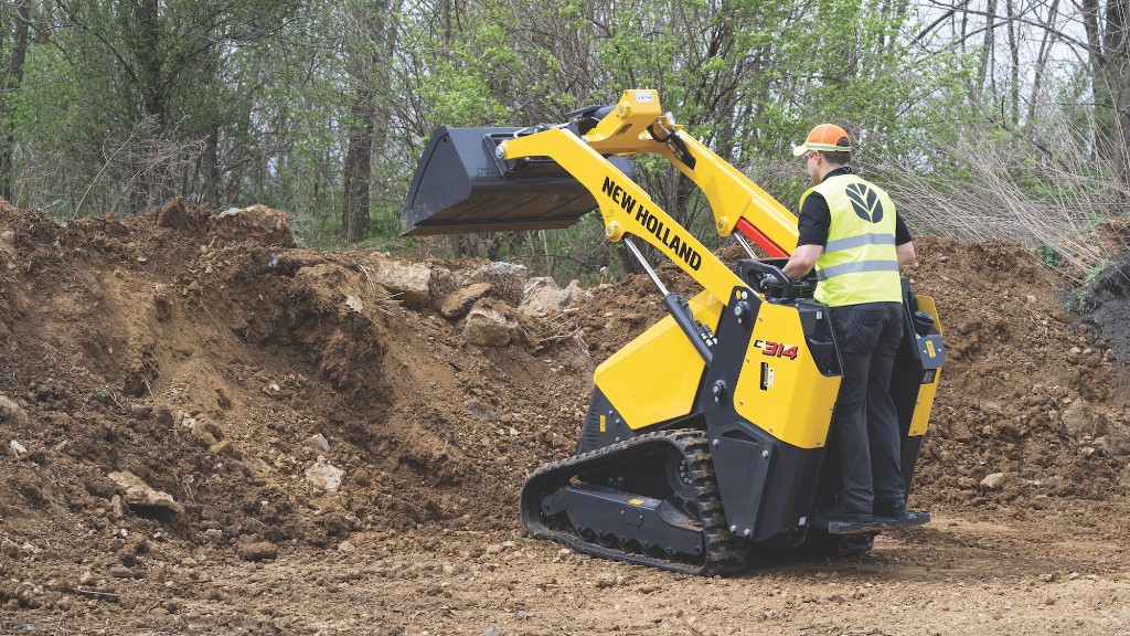 An operator dumps out a bucket of dirt while operating a mini track loader