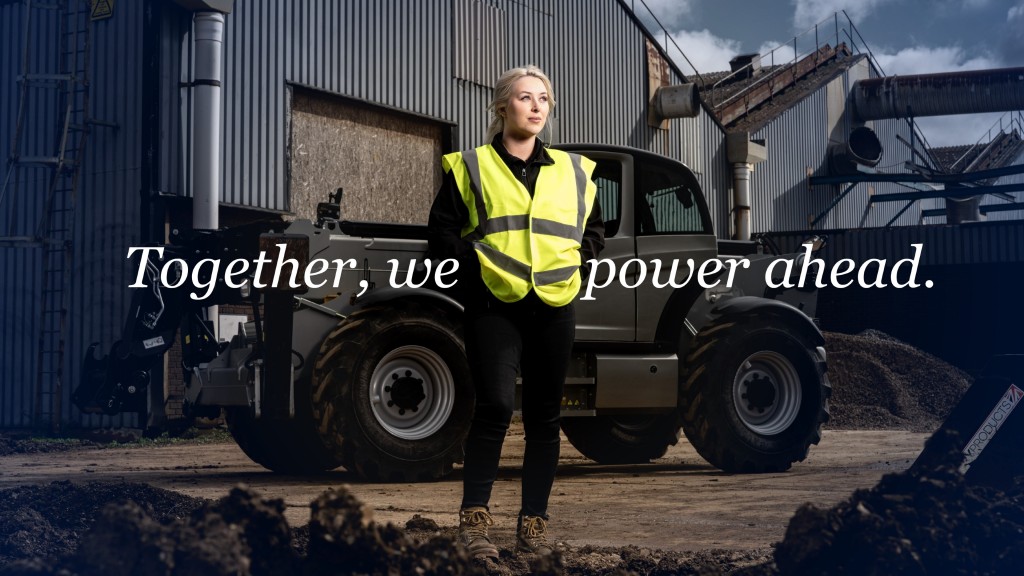 A woman in safety equipmet stands near a large facility