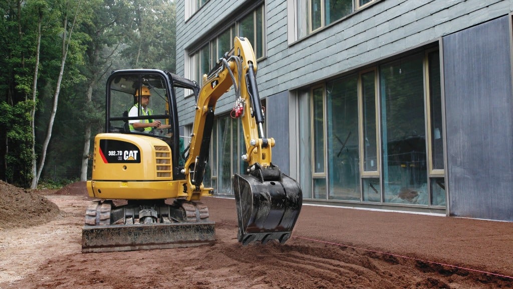 A compact excavator digs a trench near a house