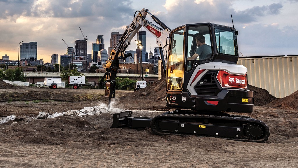 A compact excavator with a hammer attachment working on an urban job site.