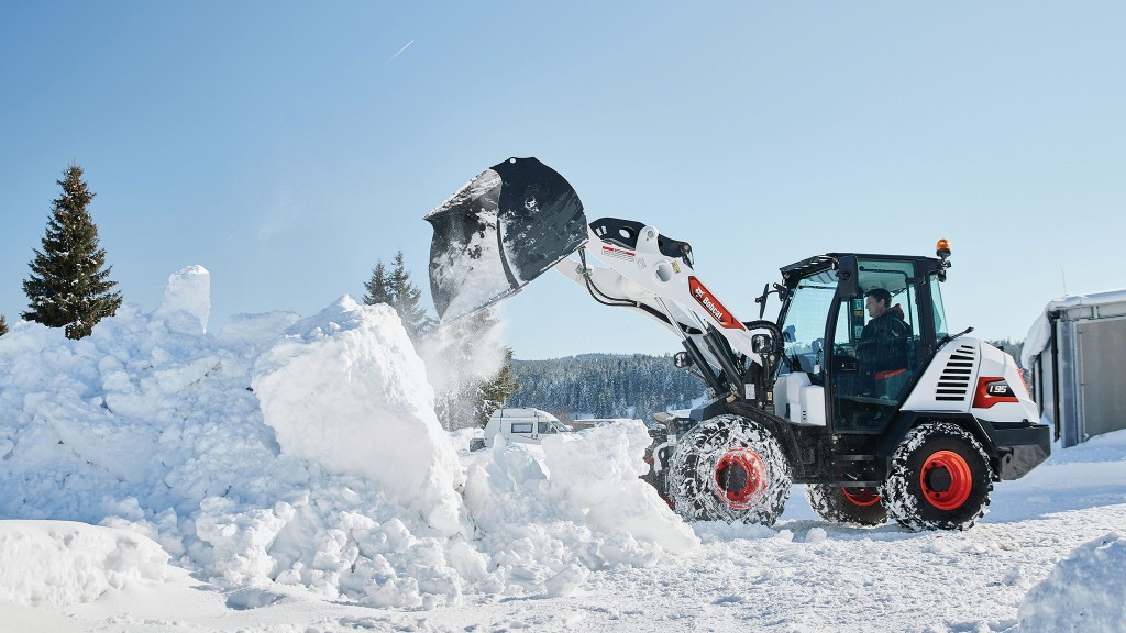 A compact wheel loader moving a bucket full of snow.
