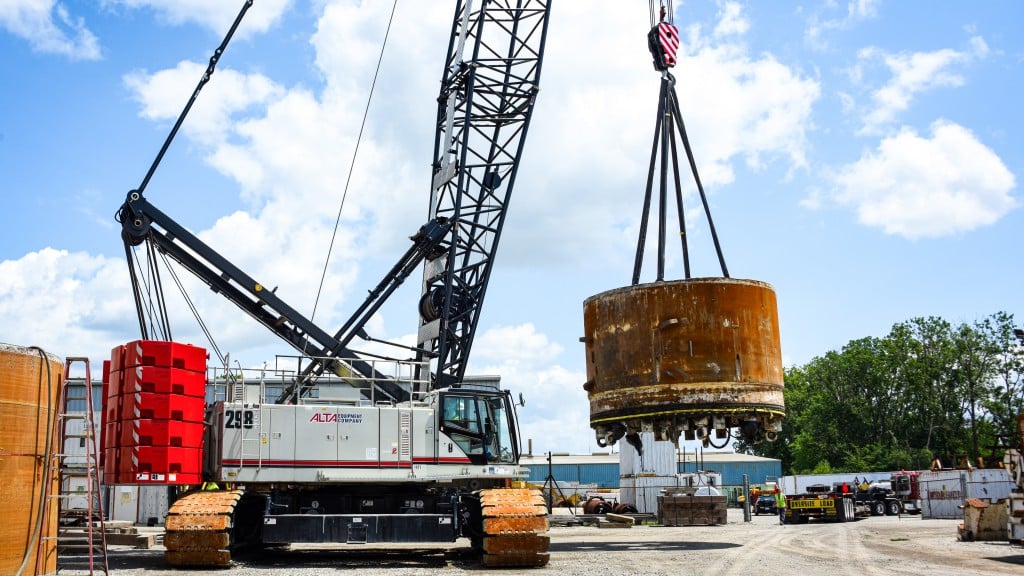 A large crawler crane moving a tunnel boring machine cutter head in a yard.