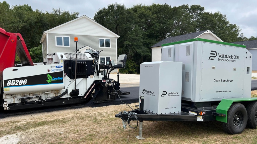 An electric asphalt paver next to a portable charger.