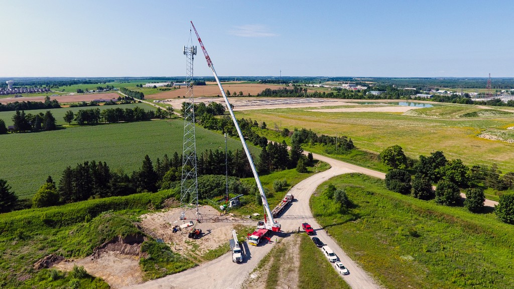An aerial view of a large crane erecting a cell phone tower in a rural area.
