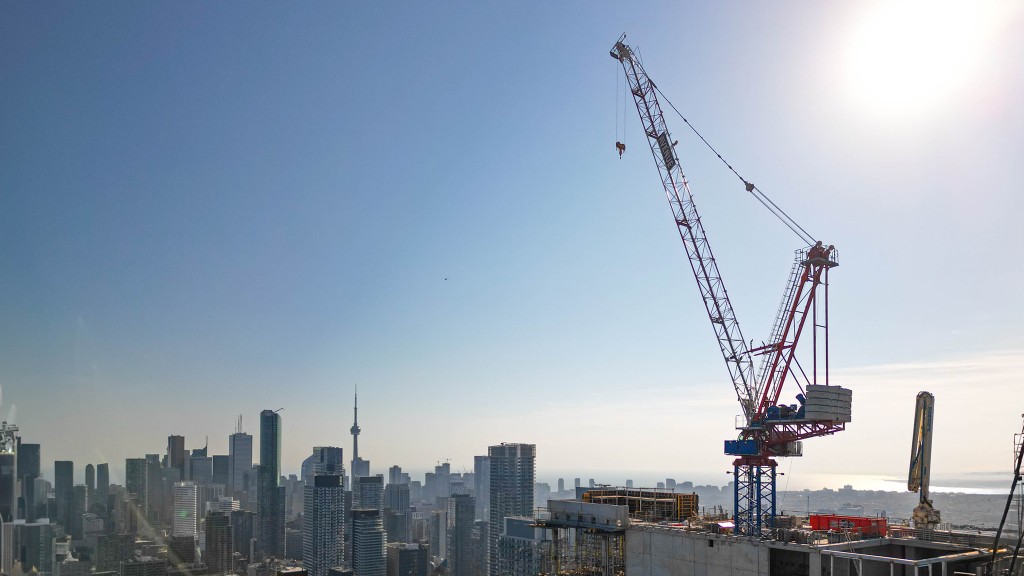 A luffing jib crane atop a tall building under construction, overlooking a cityscape.