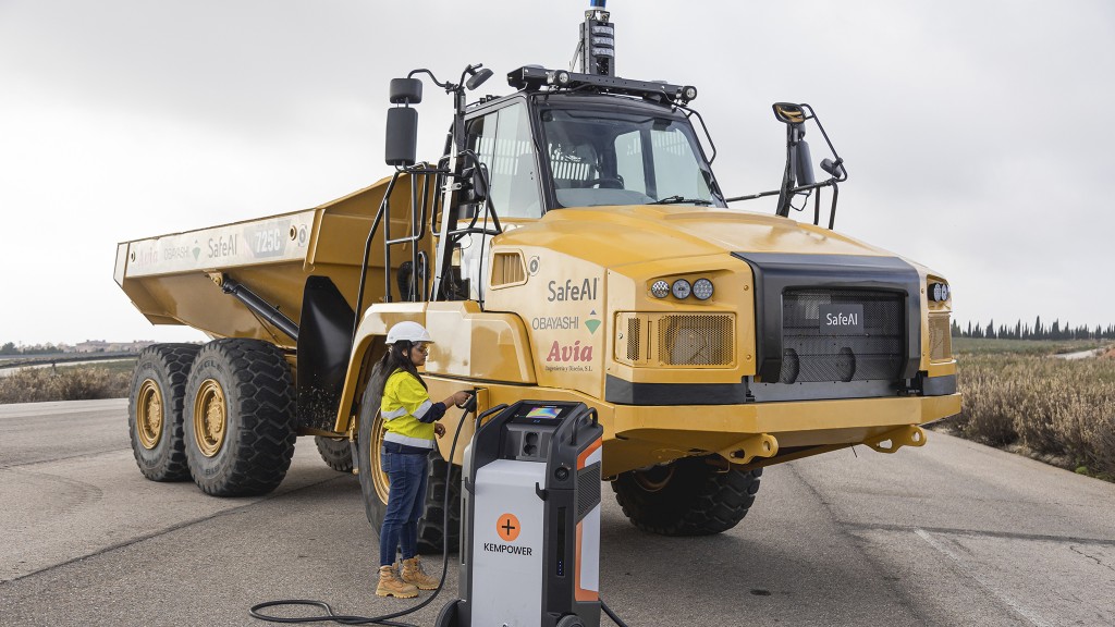 A worker plugs a charging unit into an articulated dump truck on a road.