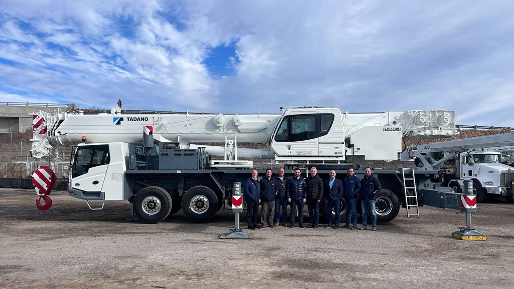 A group of people pose for a photo near a truck crane