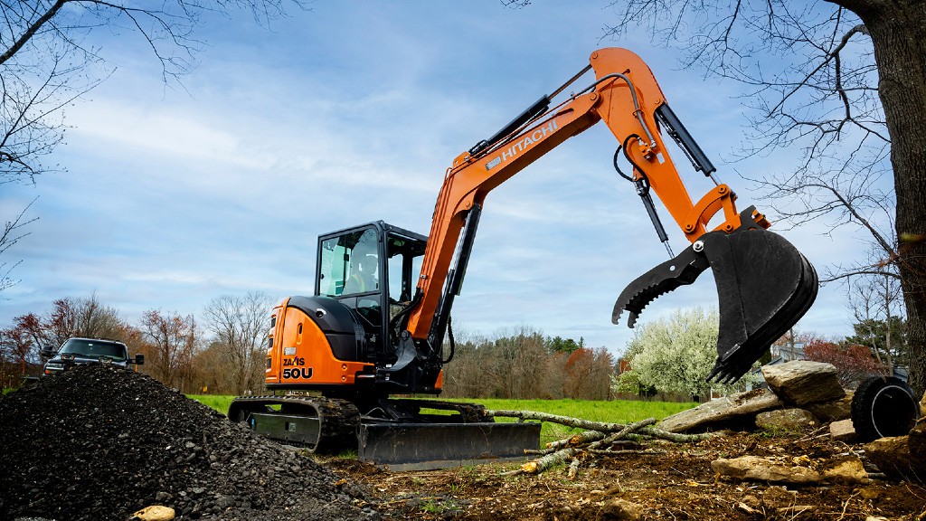 An operator operates a compact excavator on a forested job site