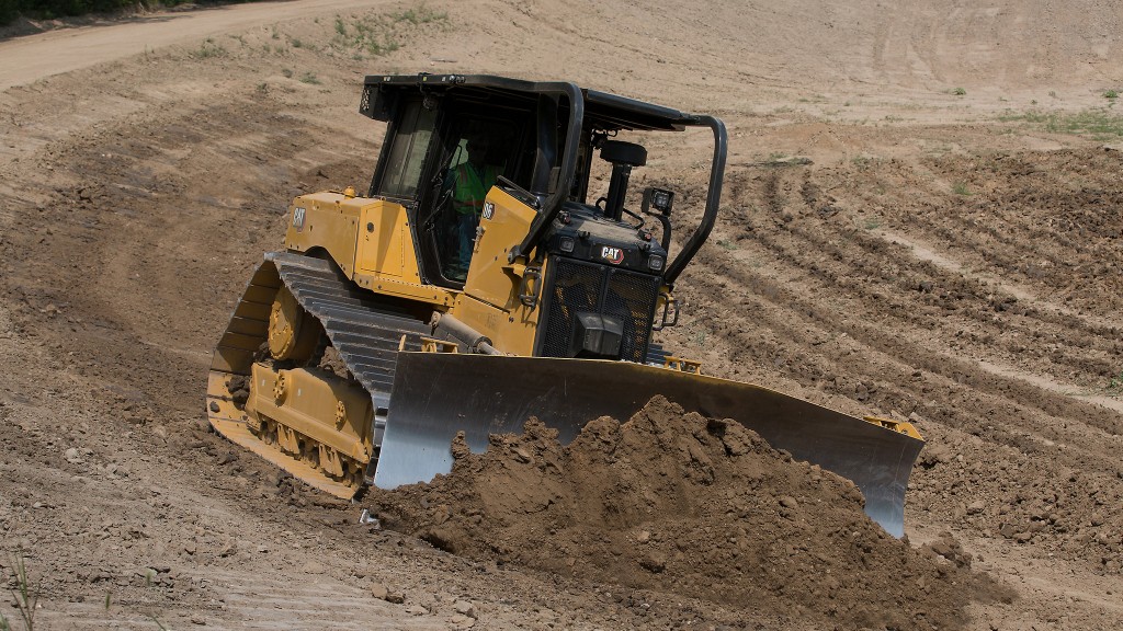 A medium dozer pushes dirt and gravel along sloped ground.