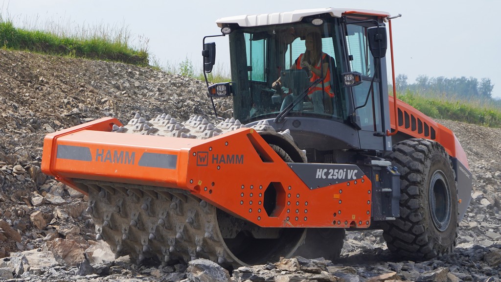 A compactor equipped with a crushing drum works on rocky ground.