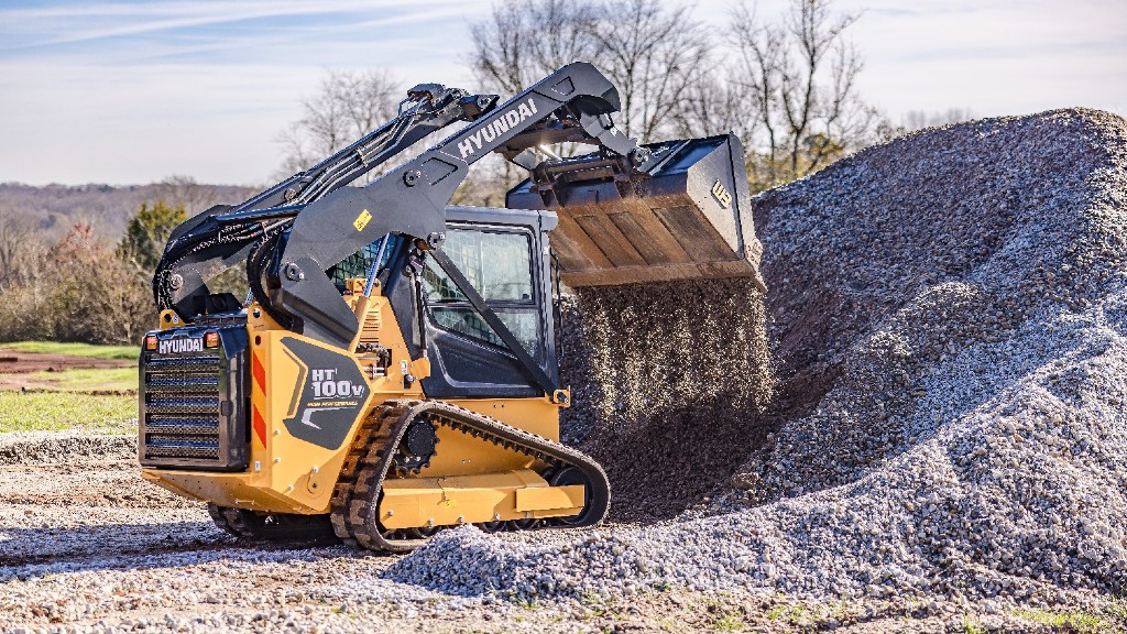 A compact track loader dumps out a bucket of gravel
