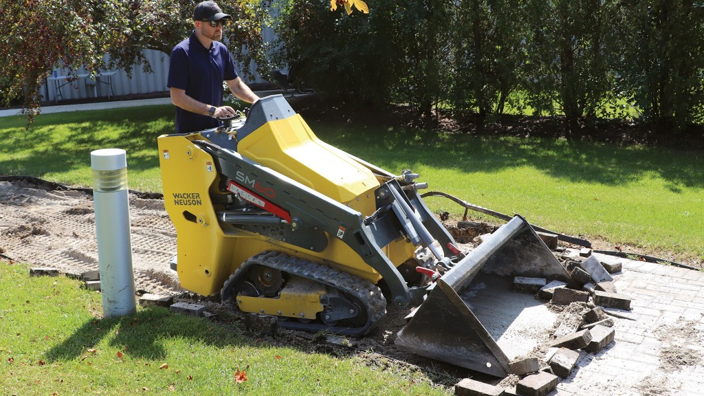 A mini track loader removes bricks from a walkway