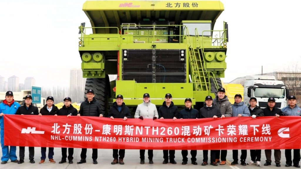 A group of factory workers stand in front of a large truck with a celebration banner.
