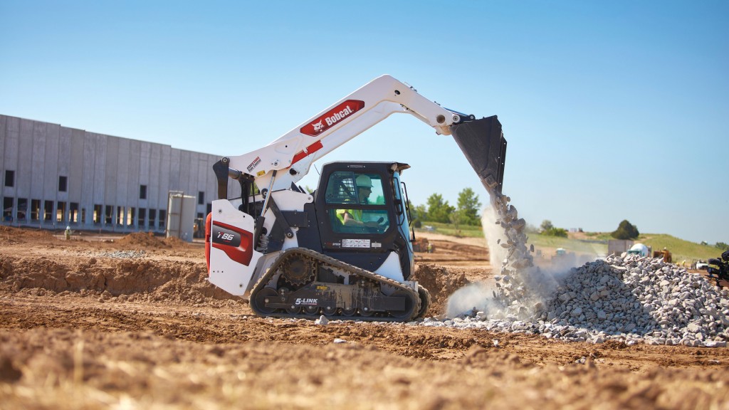 A compact track loader dumps out a bucket of rocks