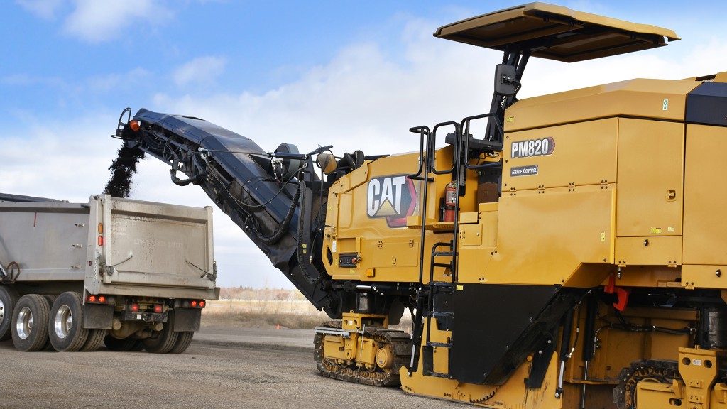 A cold planer working along a roadway, placing asphalt into a truck.
