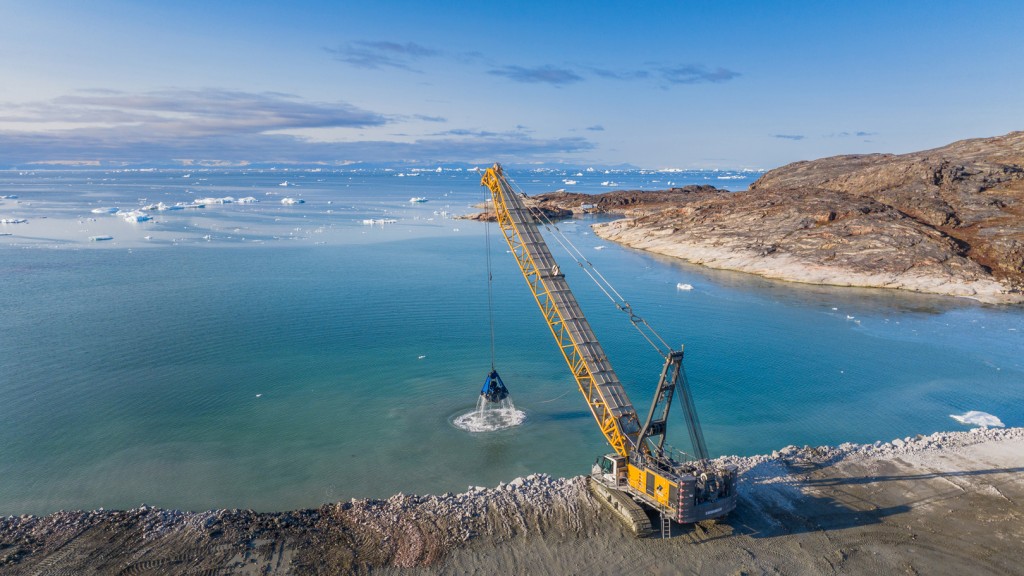 A crawler crane works at the edge of an ocean shore with ice floes in the background.