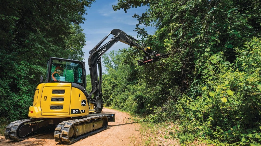 A mini excavator uses an attachment to cut overhanging brush