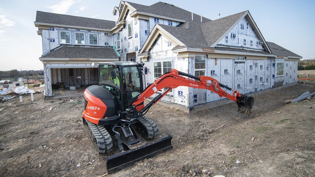 A mini excavator digs a trench near a house under construction