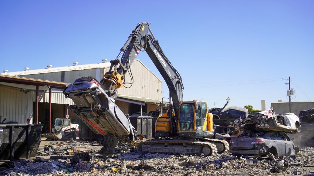 An excavator lifts a scrap car